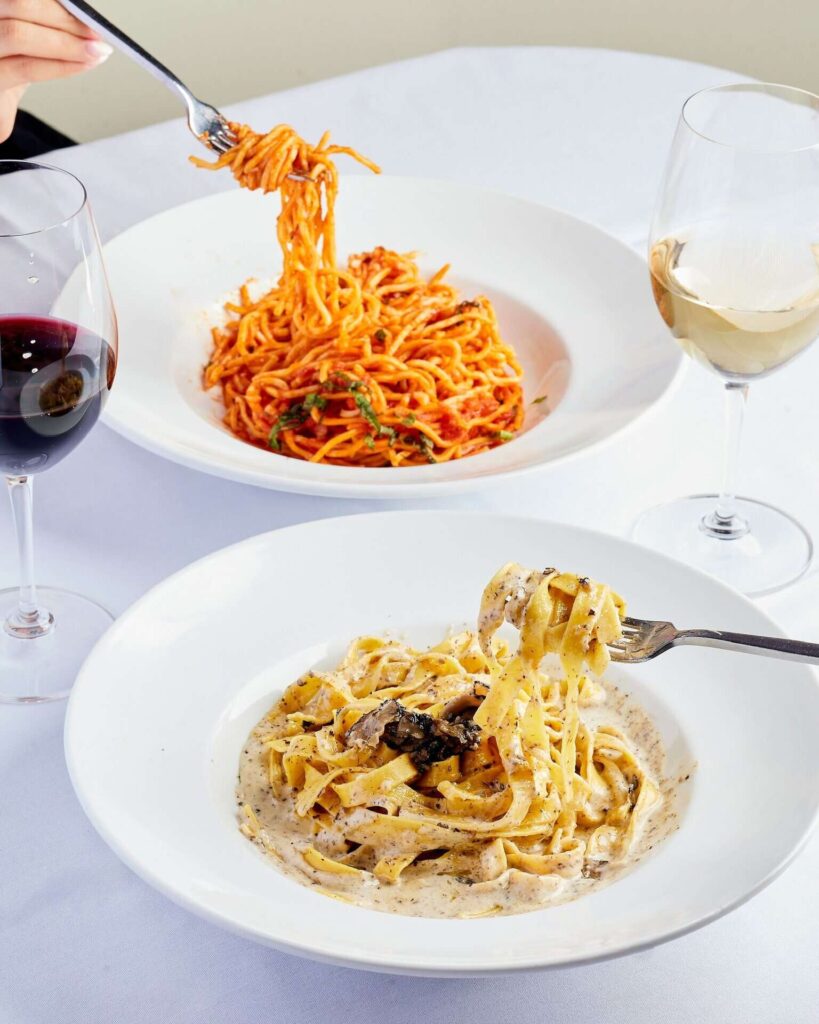 Forks twirling pasta over 2 dishes paired with red and white wine at Serafina Restaurant