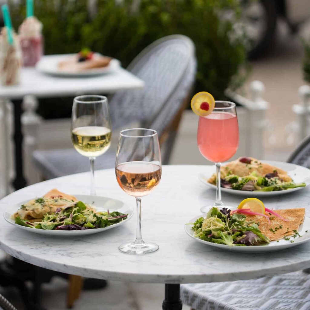 Plates of food and wine on an outdoor table at Sweet Paris Crêperie and Café