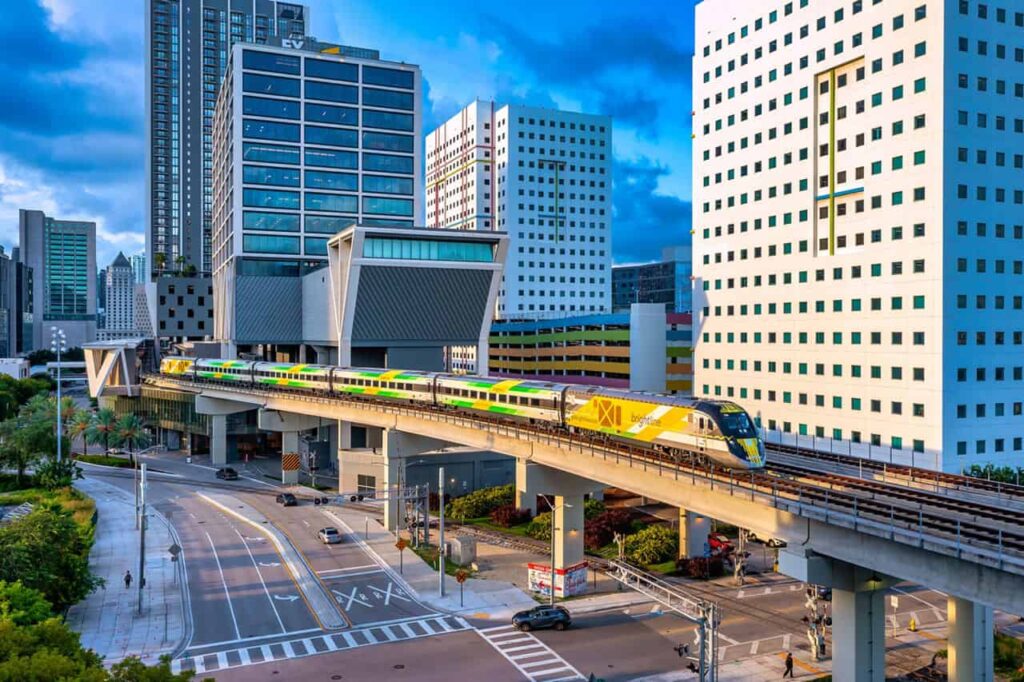 Exterior view of a Brightline train departing the Brightline MiamiCentral station on elevated tracks surrounded by downtown Miami buildings